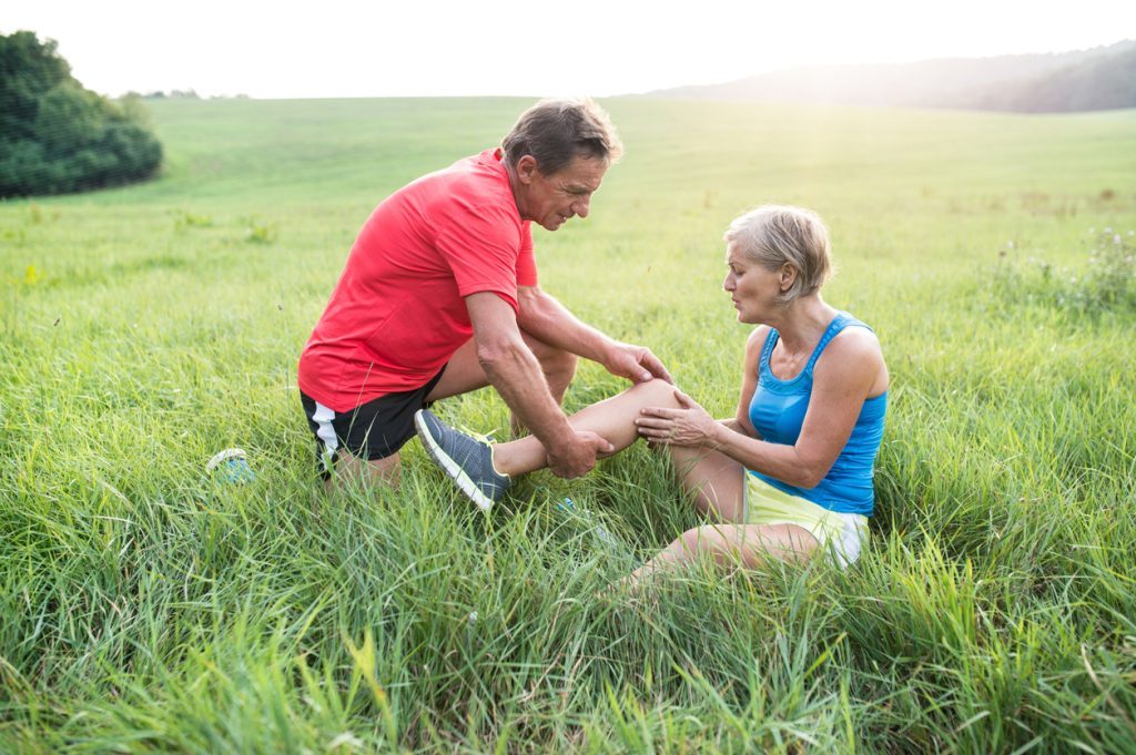 Two runners stop in sunny green field to examine one runner’s painful knee