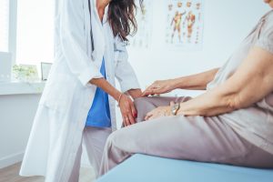 Doctor examining older patient’s knee on exam table