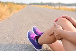 Runner on country road sitting down holding knee in pain